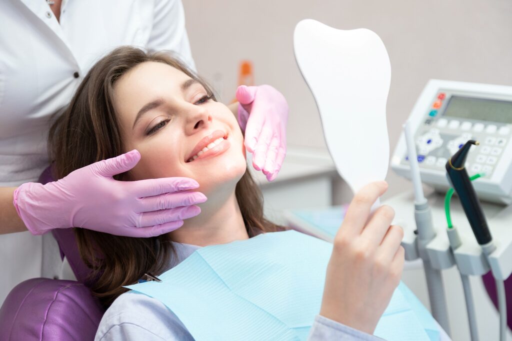 Woman in dental chair admiring her smile in handheld mirror